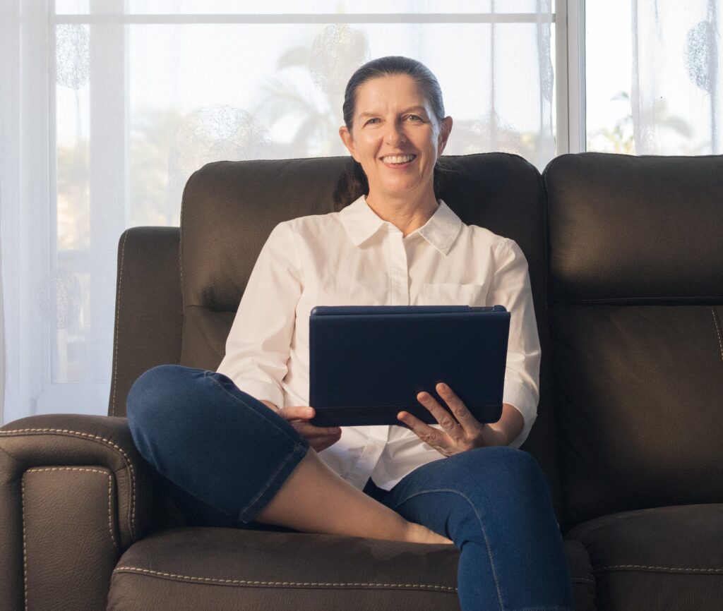 Fione Spence Mindset Coach, smiling sitting on couch with iPad